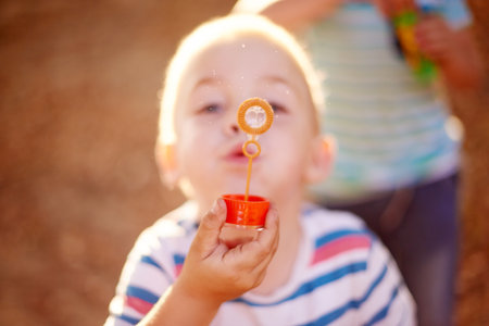 Bubbles, blowing and boy in park with play, sunset adventure and outdoor development for kids in nature. Relax, weekend and child in garden playground with soap wand, childhood games and fun activityの写真素材