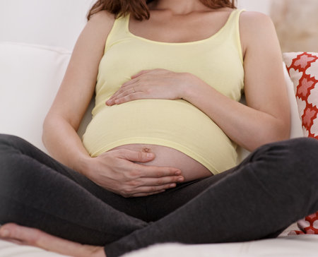 Relax, belly and pregnant woman on sofa in house for bonding, rest and prenatal connection. Health, wellness and female person holding pregnancy stomach for maternity break in living room at home.の写真素材