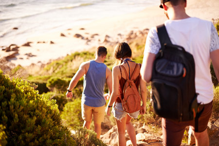 Walking, travel and back of people by beach for journey, weekend trip or adventure on seaside vacation. Discovery, fun and group of friends by ocean for holiday or getaway in nature for bonding.の写真素材