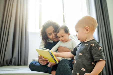 Mother, babies and learning with book in home, storytelling and education in house. Development, care and happy mama reading with children, kids or toddlers while bonding and having fun together.の写真素材