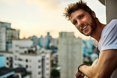 Apartment, man and happy at balcony in city on break to relax, chilling and peace in Brazil. Male person, home and portrait with smile for self care, day off and rest, comfortable with urban viewの写真素材