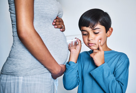Pregnant, woman and child with glass listening to baby movement, thinking and imagination. Pregnancy, mother and boy kid with stomach for sibling bonding, development and curious on studio backgroundの写真素材