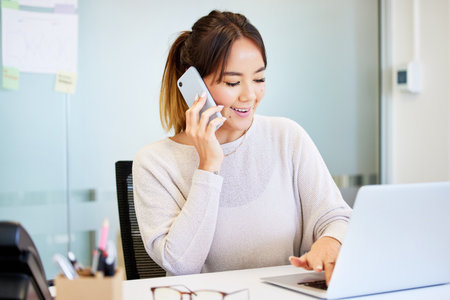 Phone call, laptop and business Asian woman in office for contact, communication or discussion. Professional, admin and person on smartphone for planning, online chat and talking to schedule meetingの写真素材