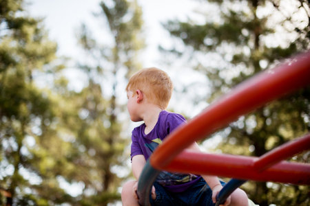 Children, merry go round and thinking with boy in forest for active play, development or growth. Adventure, balance and carousel with ginger kid having fun on playground equipment in natureの写真素材