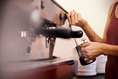 Barista, coffee machine and hands of woman in cafe to brew drink for hospitality or service. Cup, froth and milk with waitress person closeup in restaurant for preparation of cappuccino or latteの写真素材