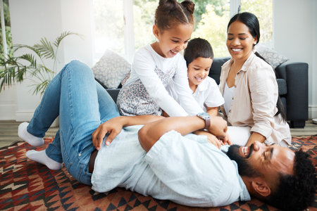 Parents, children and excited in home with game, tickling fun and bonding on weekend. Couple, kids and happy family on living room floor for relationship development, Fathers Day and playful energyの写真素材