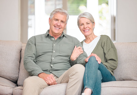 Portrait, mature couple and happy on sofa in living room at home for bonding, support and care in Germany. People, relationship and smile with confidence on couch for retirement, rest and relaxの写真素材