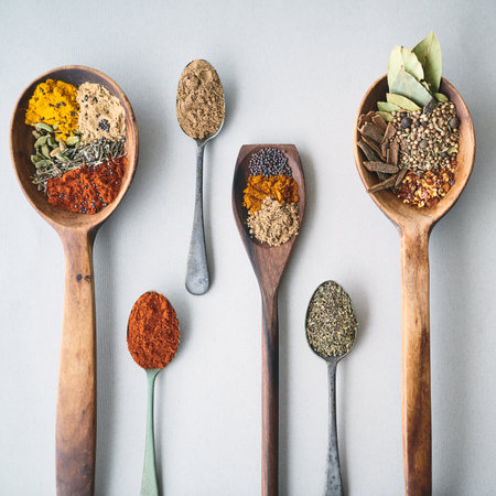 Selection, spices and seasoning in spoons for food, culinary wallpaper with herbs and powder for cooking. Above wooden utensil, aromatic and organic variety of natural ingredients on white backgroundの写真素材