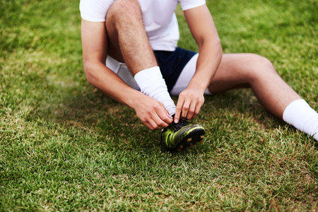 Man, hands or tying laces with shoes on grass field for sport, running or workout preparation. Male person, legs or tie soccer boots for game, match or getting ready for football practice or trainingの写真素材