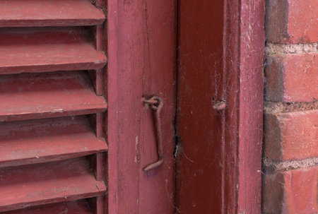 Closeup, red door and hook with lock for old exterior, damage or vintage doorframe of abandoned home. Empty, entrance or weathered wood with poor safety or scuff marks for security constructionの写真素材
