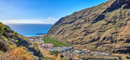 Beach, neighborhood and mountains by city for travel, outdoor holiday and weekend trip destination. Buildings, landscape and tourism with vacation location, environment and ocean scenery in Spainの写真素材