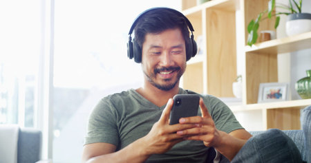 Headphones, man and typing with phone in home for music search, streaming service and audio...