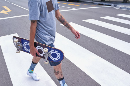 Man, hands and walking with skateboard in city on pedestrian crossing for travel, commute or journey. Male person, hipster or tourist with board for skating challenge, extreme sport or street rideの写真素材