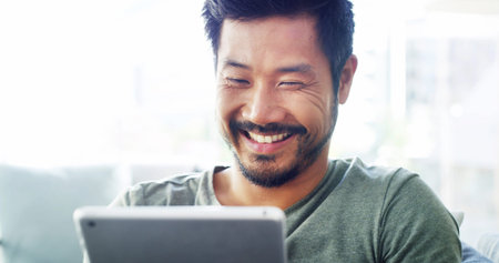 Tablet, relax and smile with Asian man on sofa for social media, streaming and networking app....