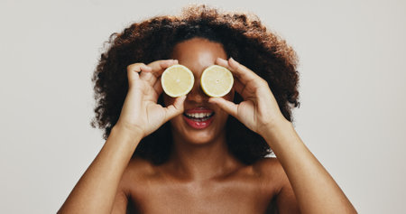 Lemon, skincare and woman with smile, studio and antioxidant benefits for smooth skin, cover and shine. White background, exfoliating and African person with cosmetics for glow, happy and modelの写真素材
