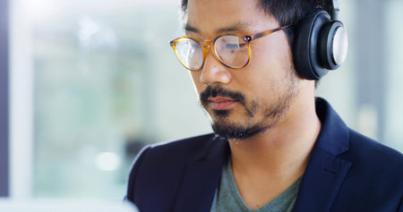Asian man, glasses and headphones with music for creative development or web design at office. Male...