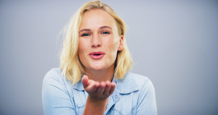 Blowing, kiss and portrait of woman on gray background with reaction for flirting, romance and pride. Mockup space, hand gesture and person with emoji for love, dating and valentines day in studioの写真素材