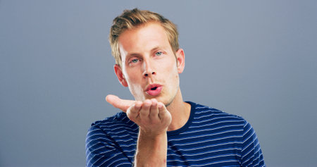 Blow kiss, studio and portrait of man with reaction for flirting, romance and affection on blue background. Space, hand gesture and isolated person with emoji for love, dating and valentines dayの写真素材