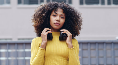 Woman, headphones and fashion in city in portrait for pride, streaming or attitude in street. Gen z girl, student and audio tech with trendy style, clothes or streetwear on urban sidewalk in Colombiaの写真素材