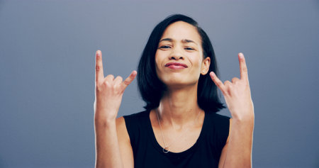 Rocker, hand and attitude with portrait of woman in studio for metal music, punk identity or crazy. Devil horn sign, edgy or funky with person on gray background space for energy, emoji or expressionの写真素材