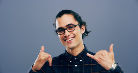 Portrait, man and call me sign at studio, symbol or connection emoji with glasses on background. Hands, smile and person with hang loose, shaka gesture or communication to get in touch with contactの写真素材
