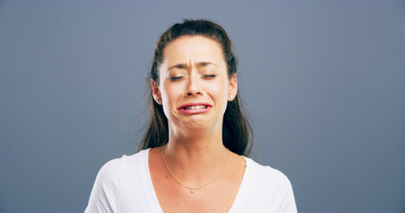 Depression, crying and anxiety with woman in studio for mental health crisis, trauma or broken heart. Unhappy face, sad or female person with bad news, stress or abuse victim on gray background spaceの写真素材