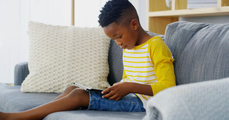 Tablet, home and child relax for reading ebook, learning app or streaming cartoon on sofa. African boy, kid and online in living room on technology to scroll entertainment, watch movies or play gamesの写真素材