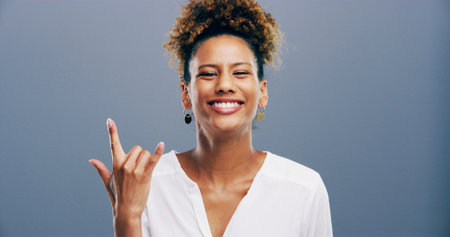 Portrait, woman and rock on sign at studio for music, heavy metal or cool emoji for culture isolated on background space. Smile, devil horns or girl with symbol, hand gesture or punk for social mediaの写真素材