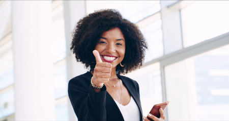 Business woman, phone and thumbs up in office lobby with social media, email or convention approval. Agreement, promotion and consultant with cellphone, mobile app and chat online for conferenceの写真素材