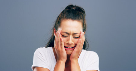 Depression, crying and stress with woman in studio for mental health crisis, trauma and broken heart. Unhappy face, anxiety and female person with bad news, sad or frustrated on gray background spaceの写真素材