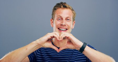 Heart hands, studio and portrait of man with gesture for support, kindness and care. Happy, confident and person with emoji, sign and hope for thank you, charity and love on blue backgroundの写真素材