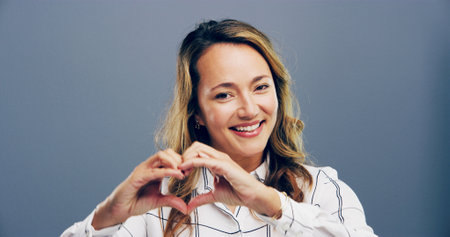 Happy, portrait and woman with heart hands in studio for appreciation, kindness and thank you. Space, person and love gesture on gray background for support, gratitude and motivation sign with smileの写真素材