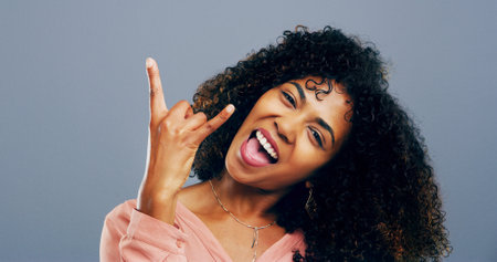 Rocker, hand and happy with portrait of woman in studio for metal music, punk identity and crazy. Devil horn sign, edgy and attitude with African person on background for energy, emoji and expressionの写真素材