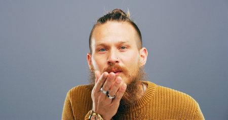 Man, portrait and blowing with kiss for love, romance or affection on a gray studio background. Male person, face or model with beard, hand or romantic gesture for distant compassion on mockup spaceの写真素材