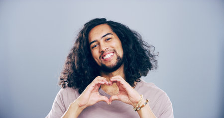 Happy man, portrait and heart hands with love shape, gesture or romance on grey background space in studio. Student person, smile and emoji or sign, symbol and kindness for valentines day mockupの写真素材