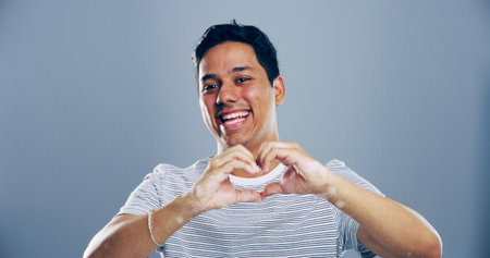 Heart hands, laughing and portrait with happy man in studio for affection, love or romance. Emoji, funny and social media with flirty person on gray background mockup for health or wellness gestureの写真素材