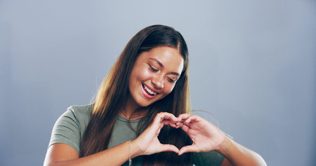 Love sign, heart hands and smile of woman for support with charity or health isolated on gray...