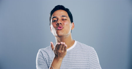 Portrait, man and blowing kiss with wink for romance, affection or love on a gray studio background. Creative, male person or model with romantic gesture, palm for distance or flirt on mockup spaceの写真素材