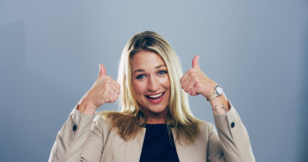 Portrait, thumbs up and woman with feedback, agreement and confidence on gray studio background. Face, person and model with hand gesture, review or icon with symbol, perfect and like with emojiの写真素材
