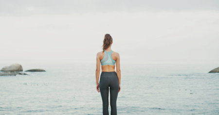 Back view, water and woman at sea for fitness, body health or thinking of wellness. Ocean, beach and calm person outdoor for exercise, planning training and peace on workout break with horizon spaceの写真素材