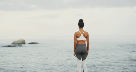 Back view, ocean and woman at beach for fitness, body health or thinking of wellness with space. Sea, water and calm person outdoor for exercise, planning and peace on workout break with reflectionの写真素材