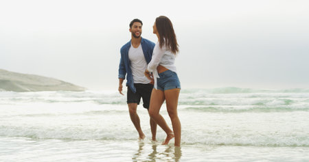 Happy couple, beach and walking together on vacation for honeymoon, holiday or bonding outdoor. Woman, man and relationship by sea for space, romantic date and care with security in commitmentの写真素材