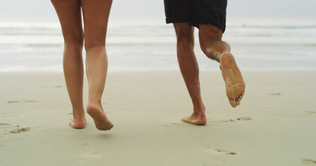People, feet and walking on beach sand for holiday, weekend or vacation together in nature. Closeup, legs and barefoot with water, ocean coast or sea waves for fun day, playful or outdoor bondingの写真素材