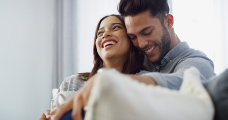 Hug, laughing and couple with coffee, house and love in living room with woman, comfortable and bonding. Happy, man and relax with partner in lounge, tea and chilling in home, embrace or relationshipの写真素材