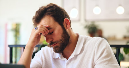Frustrated, tired and man in cafe with stress, mistake or overwork with burnout. Headache, pressure and person in coffee shop with fatigue, brain fog and freelancer with bad news for crisis on laptopの写真素材