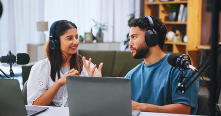 Laptop, microphone and podcast with couple in home living room for live broadcast or recording. Computer, conversation or streaming with man and woman influencer in apartment for subscription serviceの写真素材