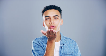 Portrait, man or blowing with kiss for love, affection or romance on a gray studio background. Creative, male person or model with romantic gesture or palm for care, distance or flirt on mockup spaceの写真素材