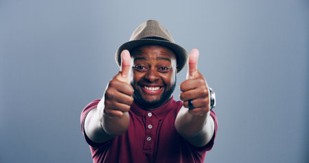 Happy, black man or portrait with thumbs up for approval, success or good job on a gray studio background. Face, male person or model with smile, like emoji or yes sign for winning on mockup spaceの写真素材