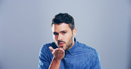 Portrait, man or blowing with kiss for romance, affection or love on a gray studio background....