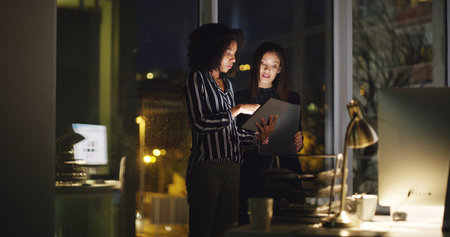 Office, business people and women with tablet at night, research information and deadline for news. Working late, teamwork and journalists with digital for article post, newsletter and proofreadingの写真素材